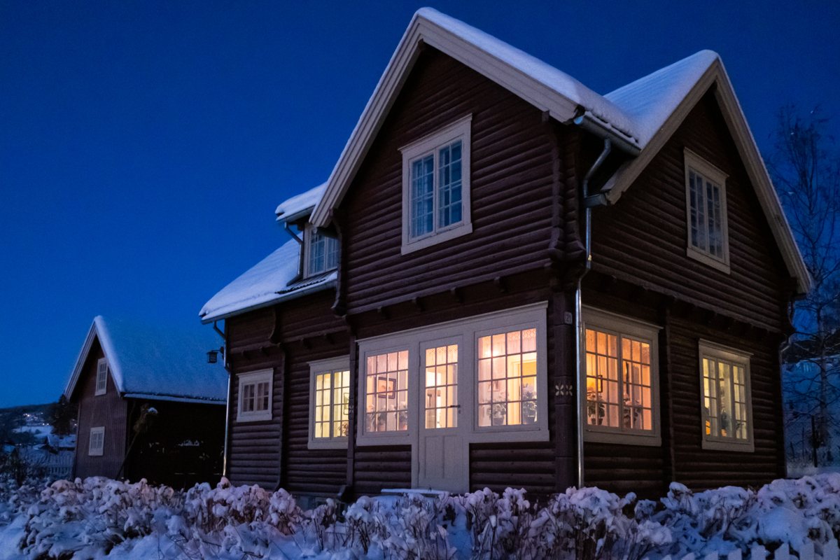 Rødmalt tømmerhus med lys i vinduene i blåtimen.